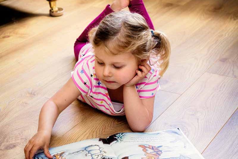 A child lying and reading on a floor with underfloor heating